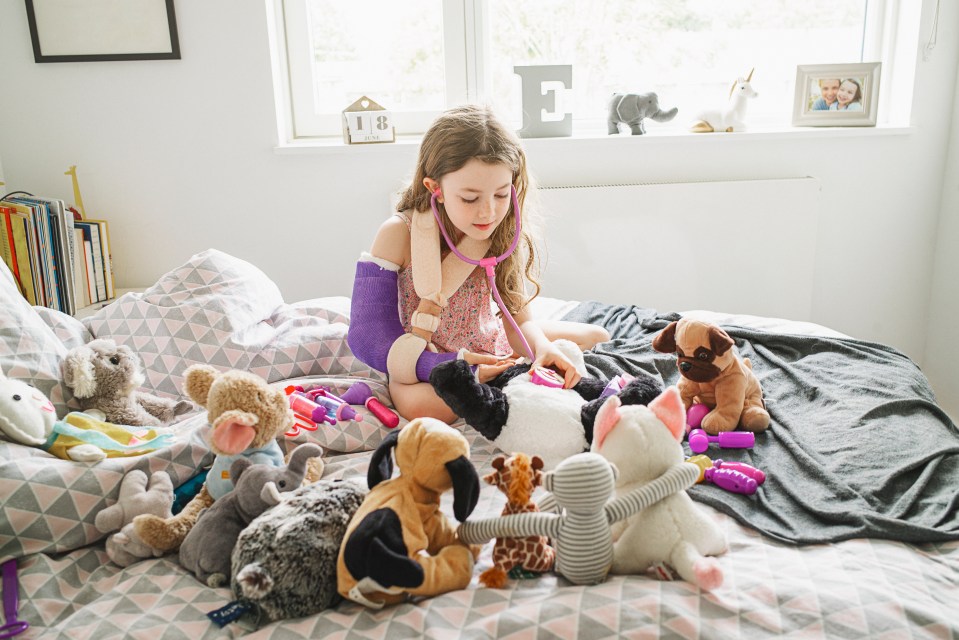 Girl with broken arm playing doctor with stuffed animals.