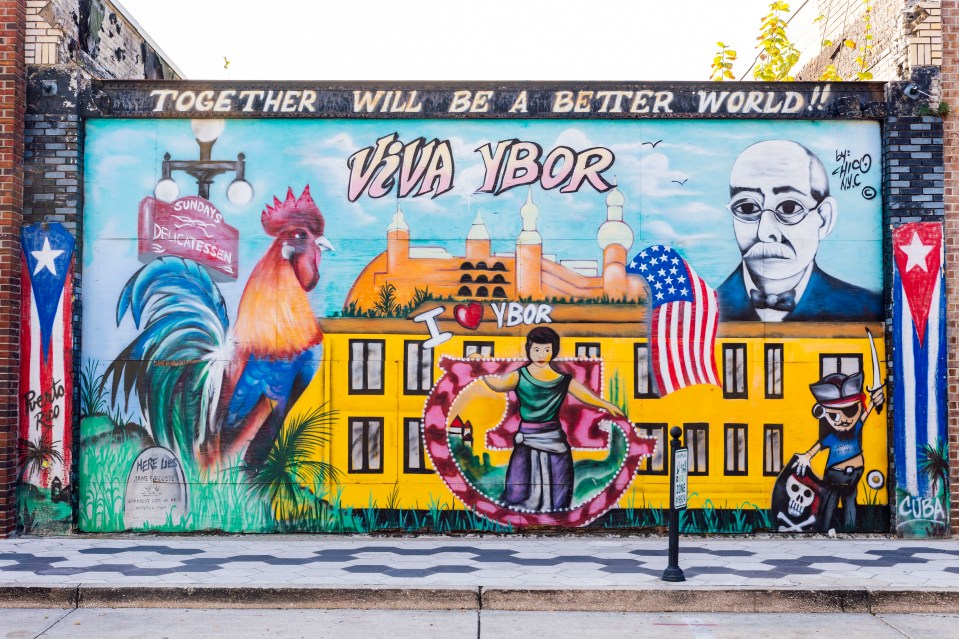 Mural depicting Ybor City, featuring a rooster, flags, and portraits.