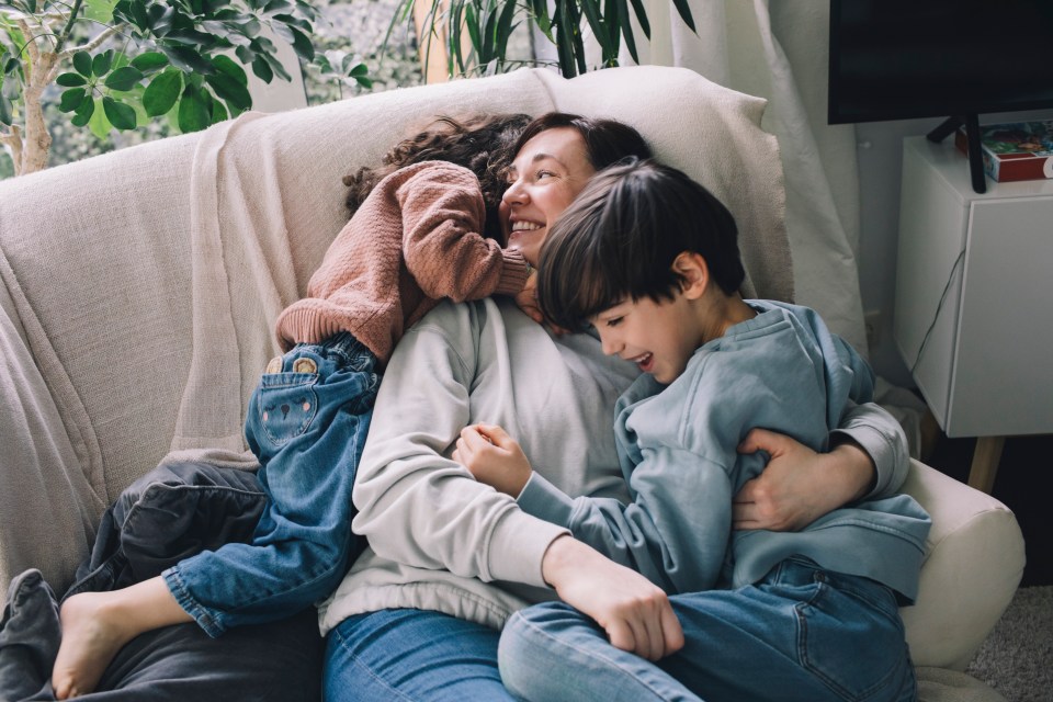 A mother cuddling her two children on a couch.