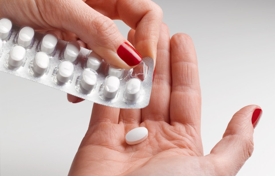 A woman's hand taking a pill from a blister pack.