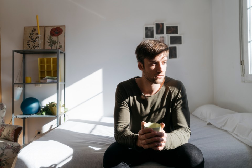 Man sitting on a bed holding a coffee cup.