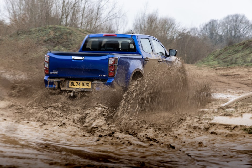 Blue pickup truck splashing through mud.