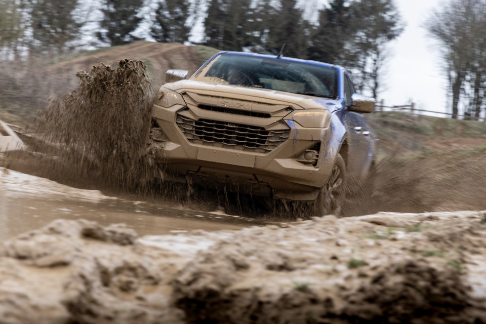 A blue pickup truck splashing through mud.