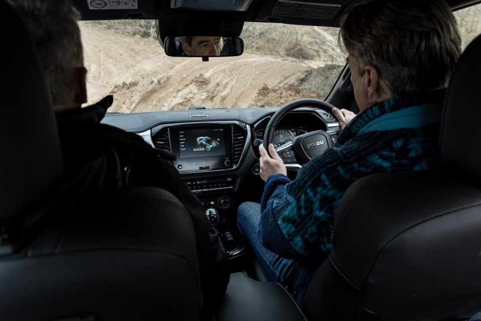 Two people driving an Isuzu on a dirt road.