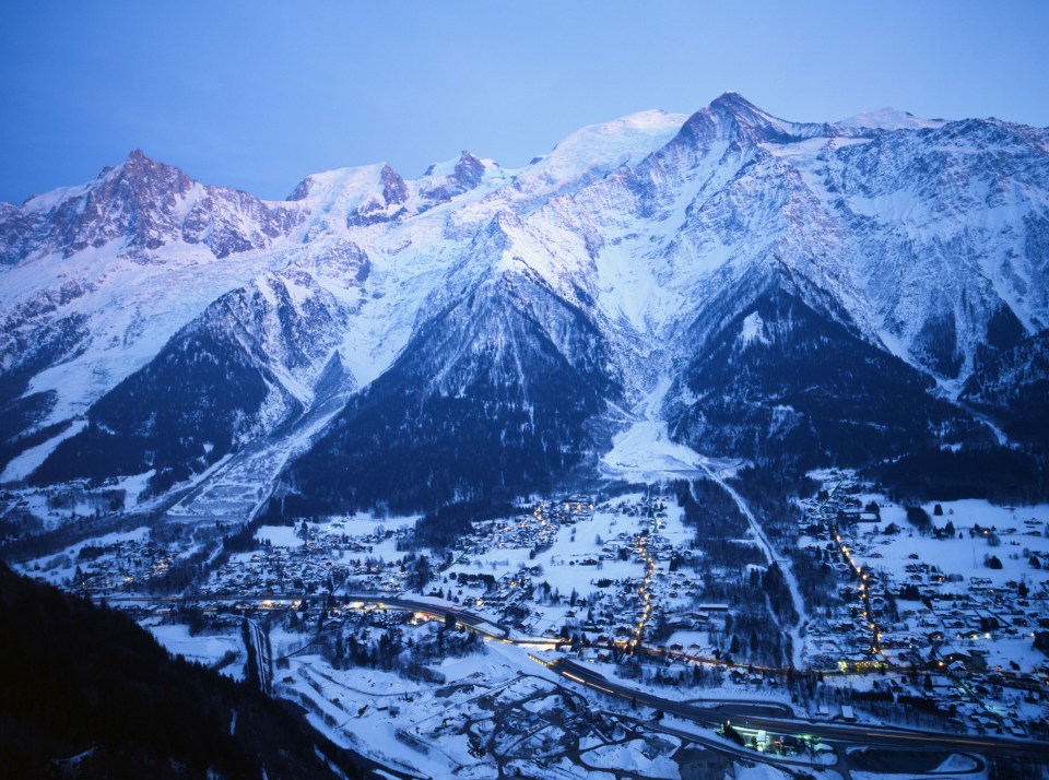 Snow-covered village at the foot of a majestic, illuminated mountain range at night.