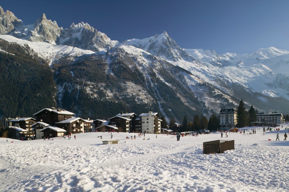 Snowy mountain valley with ski resort buildings and people sledding.