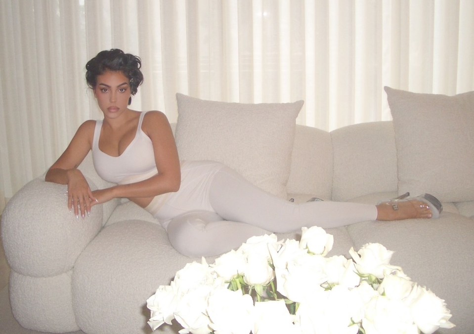 Woman in white outfit reclining on a white couch with white roses in the foreground.