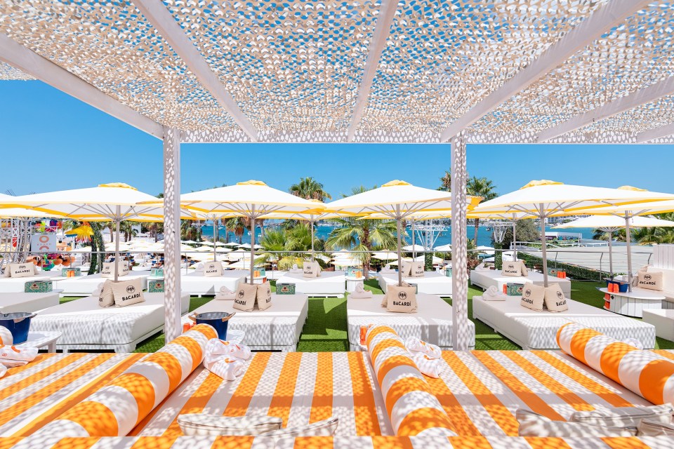 Beach club with orange and white striped lounge chairs and Bacardi-branded pillows under a white canopy.