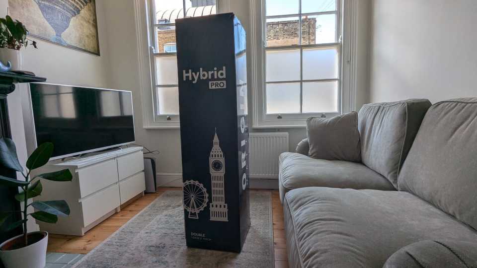 A tall box containing a double Hybrid Pro mattress stands in a living room.