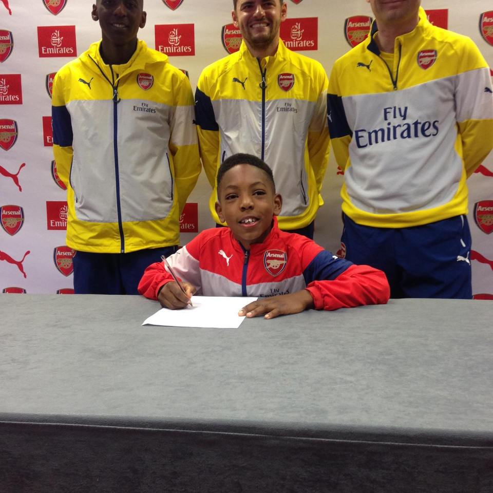 Boy signing Arsenal jersey with team members.