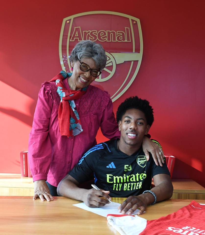 A young man signing an Arsenal jersey with his grandmother.