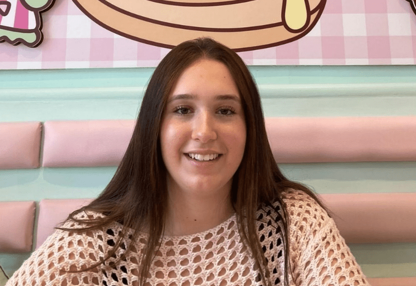 Woman smiling in front of a pastel-colored wall.