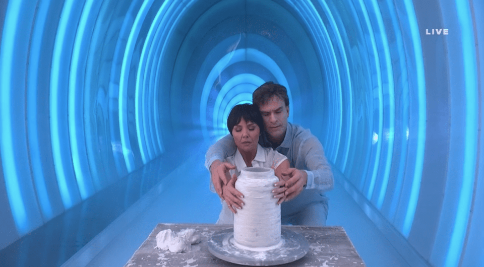 Screenshot of a man and woman working together on a pottery piece in a blue-lit tunnel.