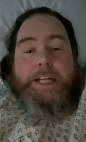 Close-up of a man with a beard lying in a hospital bed.