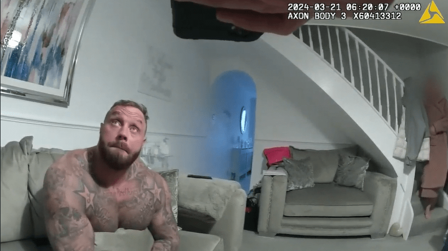 Screenshot of a tattooed man sitting on a couch, looking upward.