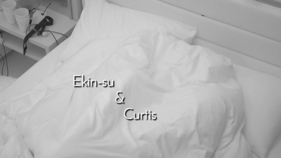 Ekin-su and Curtis under covers in bed.