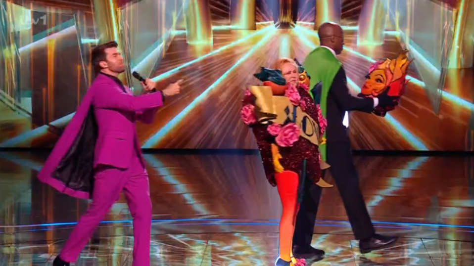 Screenshot of a masked singer being unmasked on a game show.