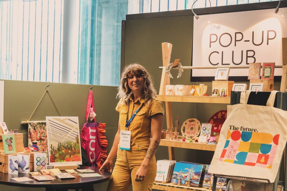 Woman at The Pop-Up Club merchandise stand.