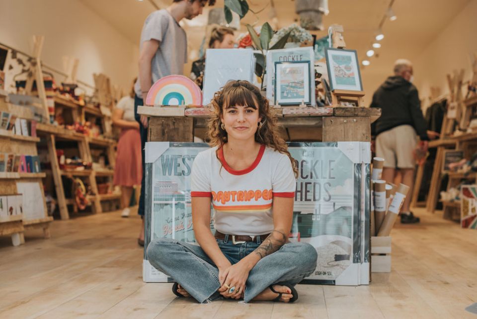 Woman sitting cross-legged in a shop, surrounded by merchandise.