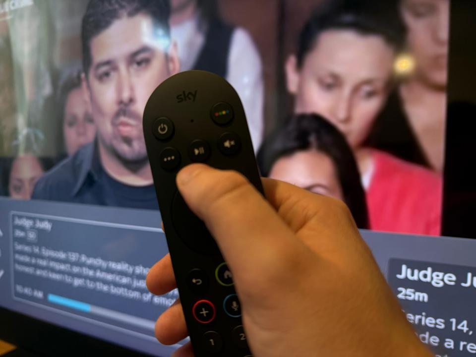 Hand holding a Sky remote control in front of a TV screen showing Judge Judy.