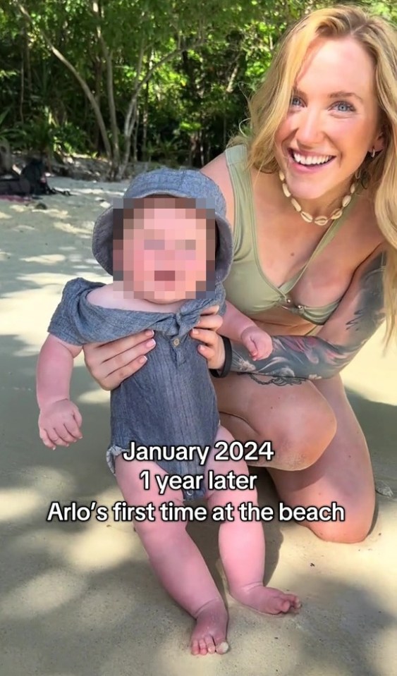 A woman holds a baby on a beach.