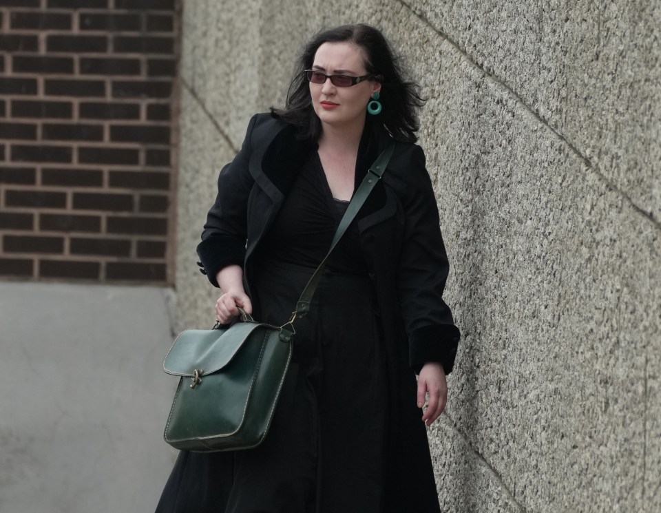 Woman in black coat and sunglasses carrying a green bag outside a courthouse.