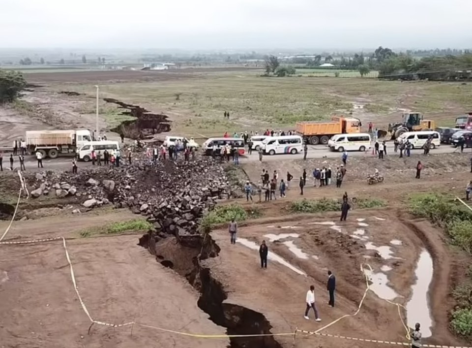 A large crack in a road, with people and vehicles stopped nearby.