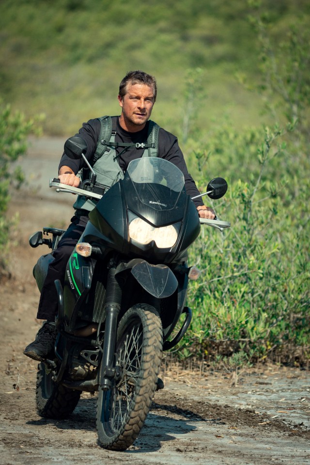 Bear Grylls riding a motorcycle.