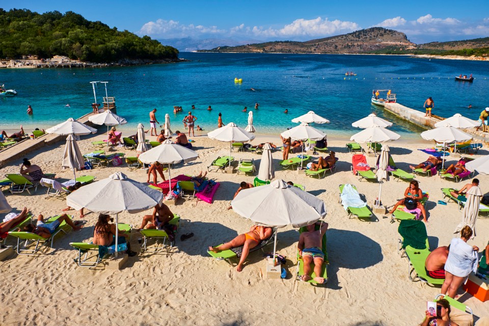 Crowded beach in Ksamil, Albania, with people relaxing under umbrellas.