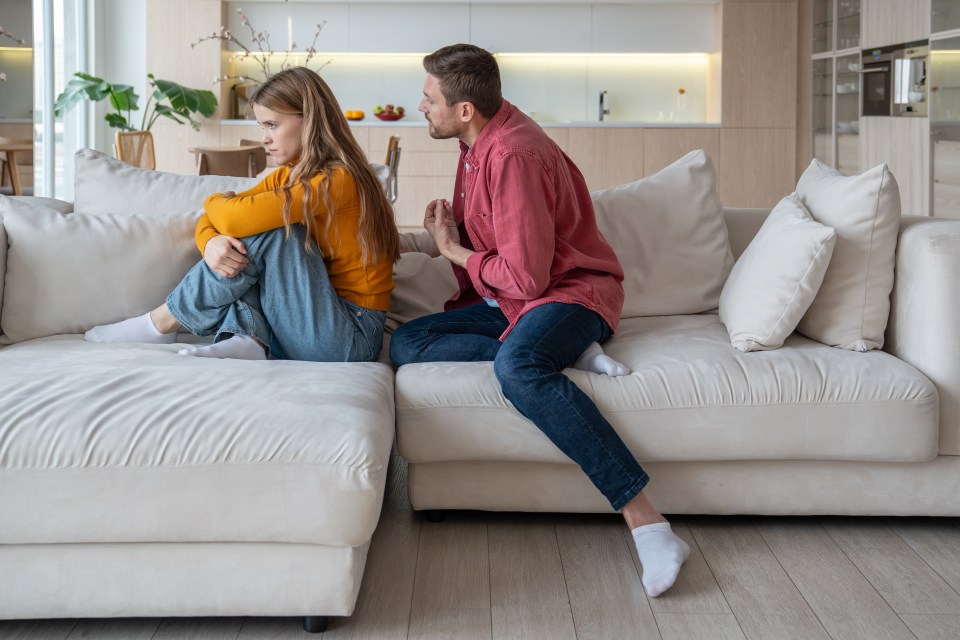 A woman sits on a sofa ignoring a man who is talking to her.