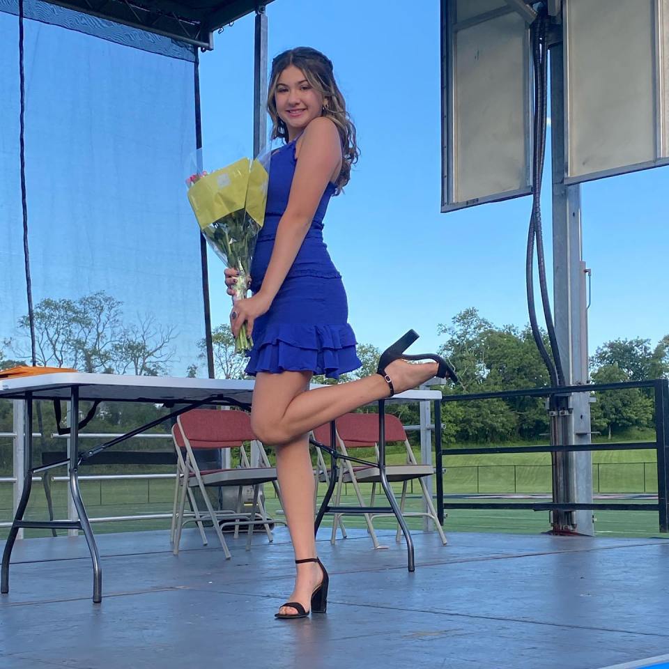 Teen girl in blue dress holding flowers on stage.