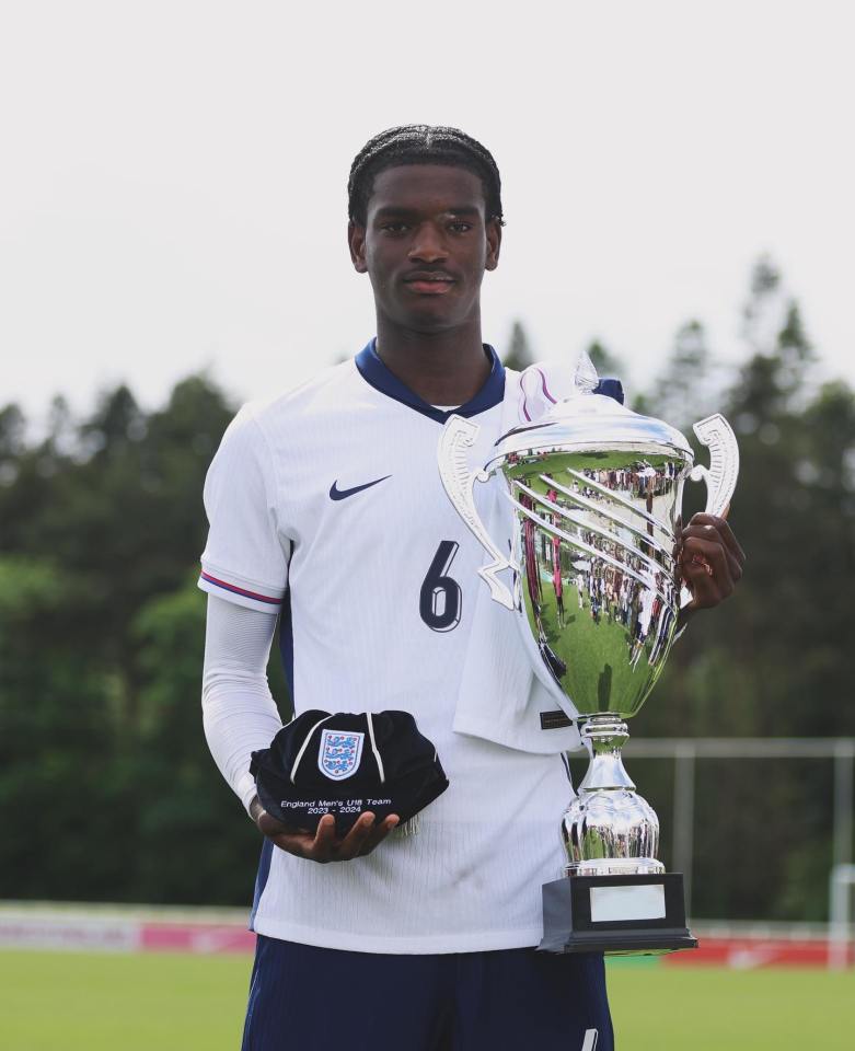 Soccer player holding trophy and cap.