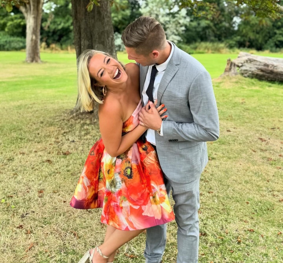 A woman in a floral dress laughs as a man in a gray suit embraces her.