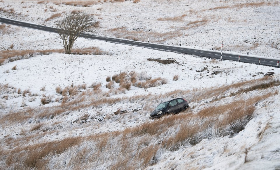 Car crashed in snowy field near a road.