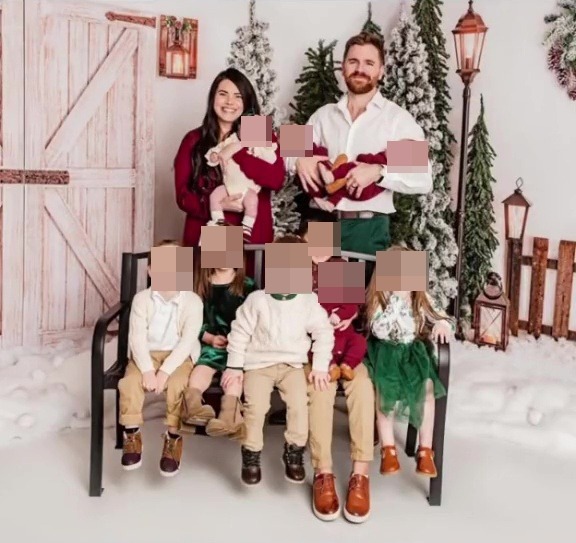 Family portrait of parents with nine children in front of a Christmas backdrop.