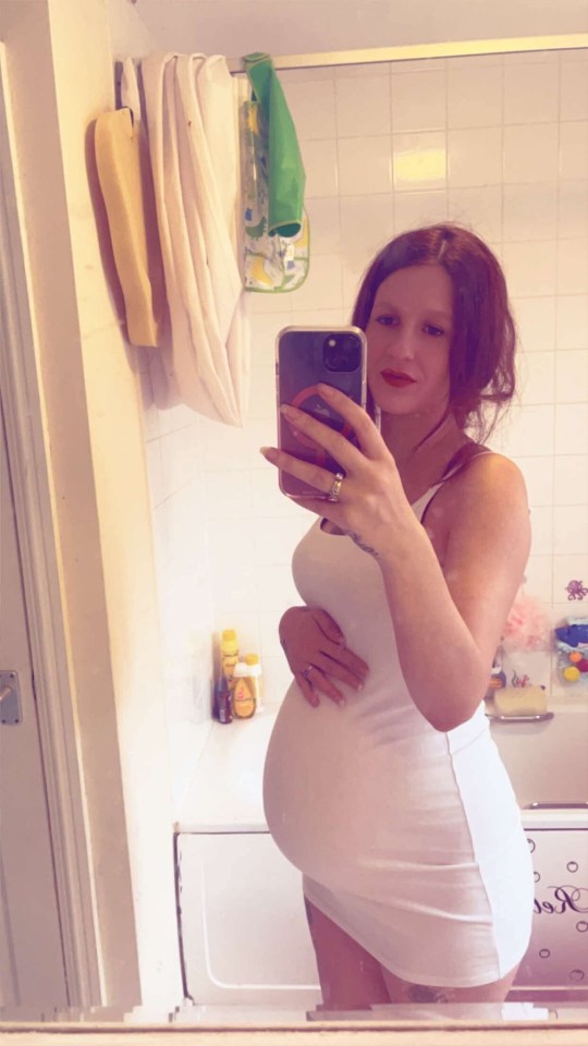 Pregnant woman taking a selfie in a bathroom mirror.