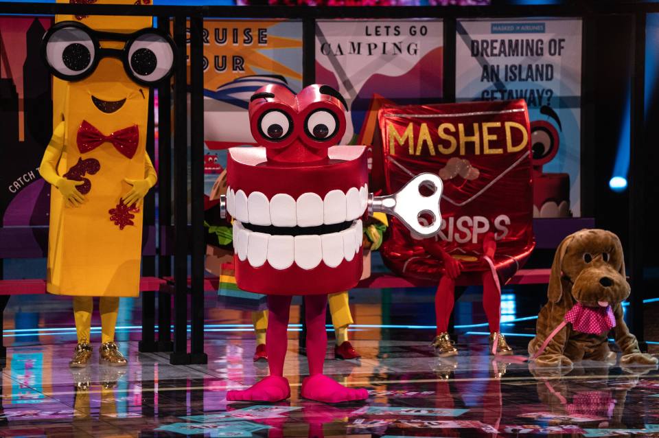 Costumes of a chattering teeth toy, a crayon, and a dog on a game show stage.