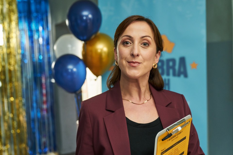 Natalie Cassidy in a maroon jacket holding a clipboard.