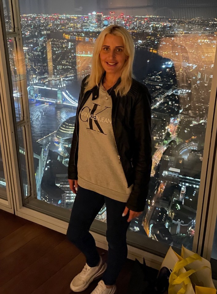 Woman standing in front of a window overlooking a city at night.