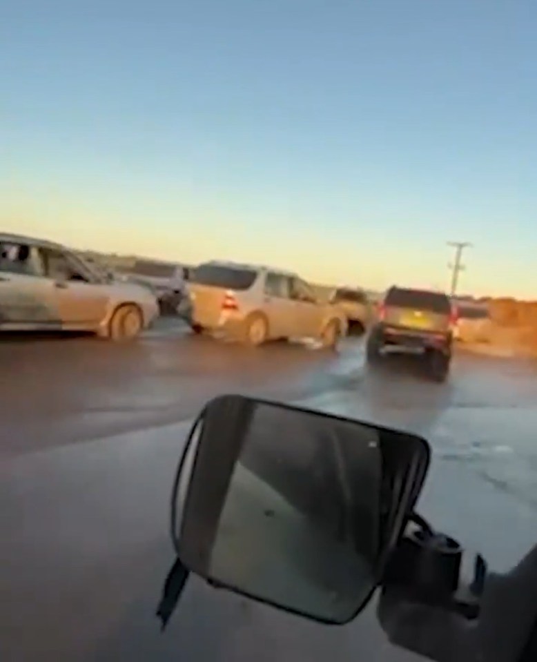 Several muddy SUVs driving on a dirt road.