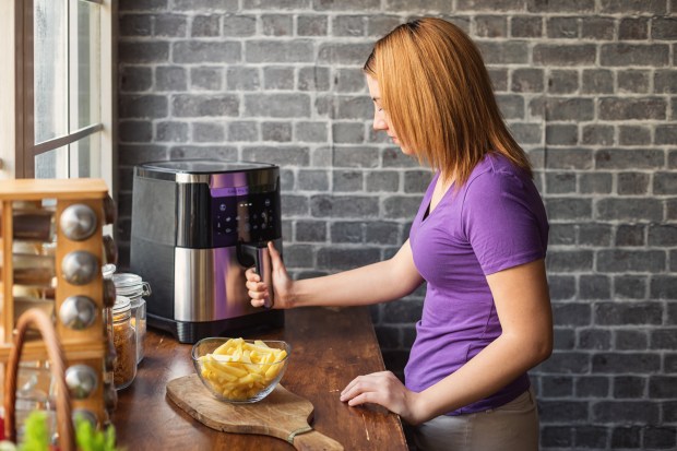 Teenage girl using an air fryer to make french fries.