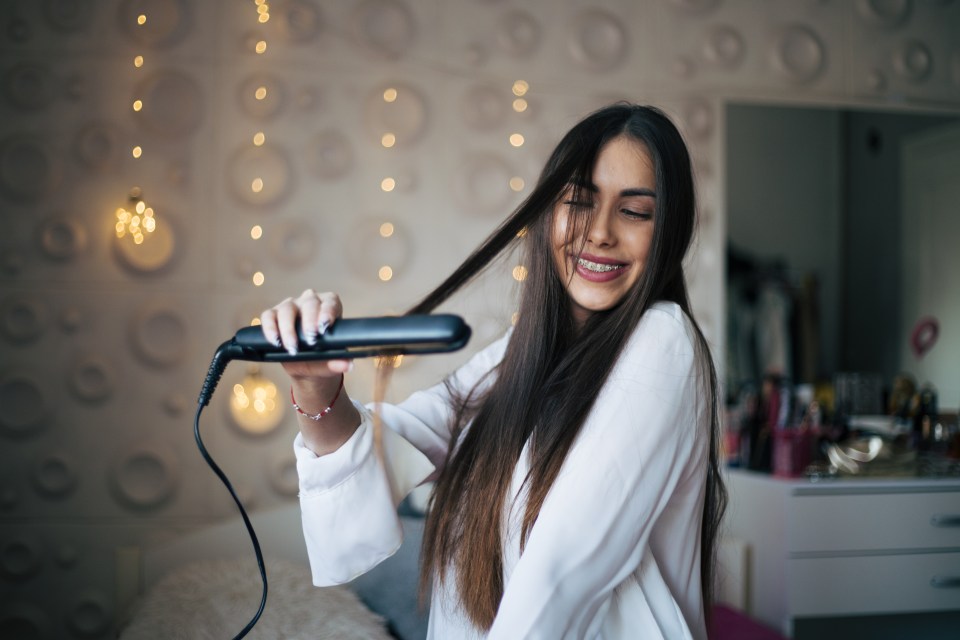 Woman straightening her hair with a flat iron.