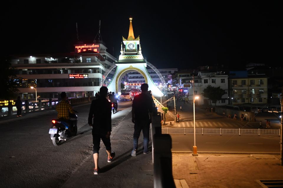 Nighttime street scene in Mongla, Myanmar, showing people walking near a clock tower.