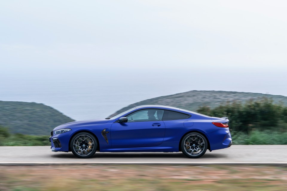 Blue BMW M8 Coupe driving on a coastal road.