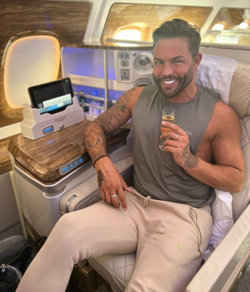 Man smiling and holding a glass of champagne while seated in a first-class airplane seat.