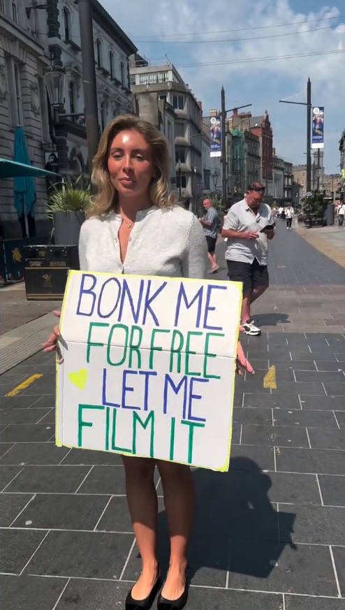 Woman holding a sign that says "Bonk me for free, let me film it."