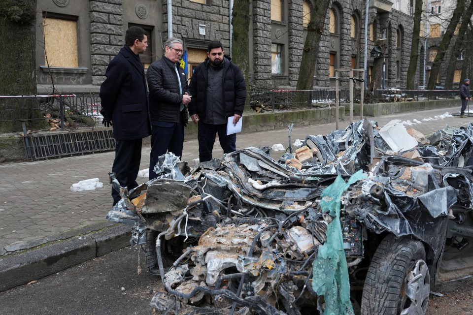 Three men inspecting a severely damaged vehicle.