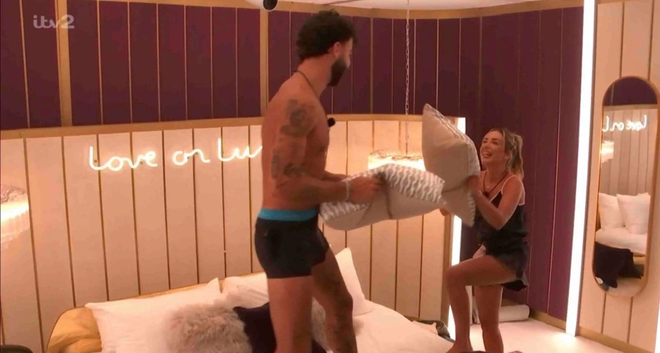 A man and woman having a pillow fight in a bedroom.