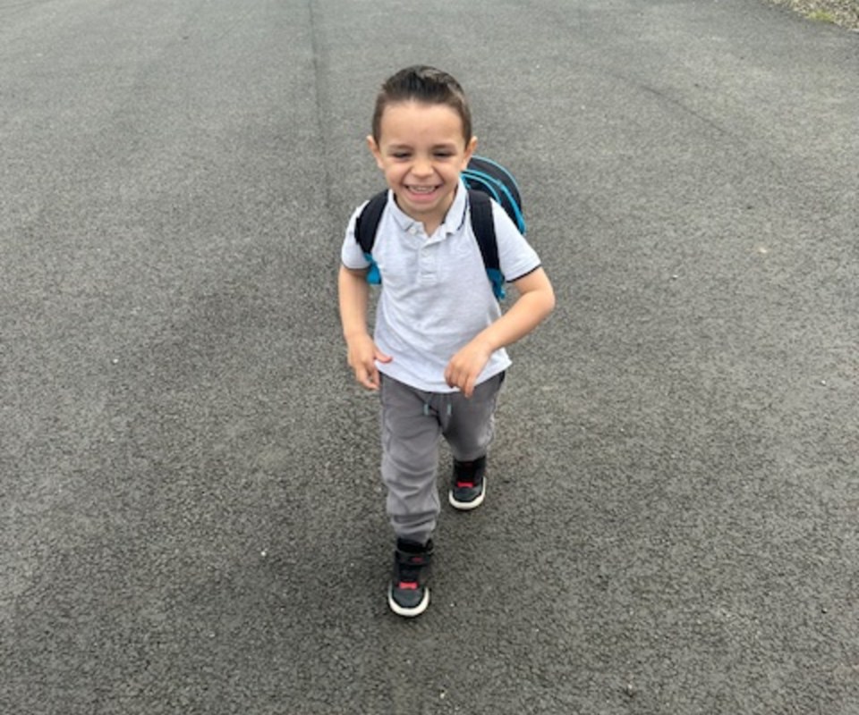 A young boy with a backpack smiles while walking on a paved path.