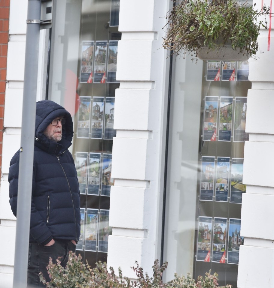 Man in a hooded jacket looking at real estate listings in a window.